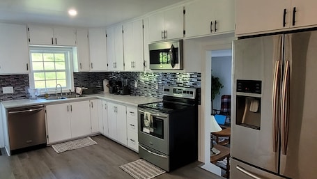 A modern kitchen with white cabinets, stainless steel appliances, a black microwave, and a built-in oven.
