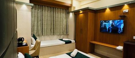 A hotel room with two beds, a TV, a desk, and a seating area.