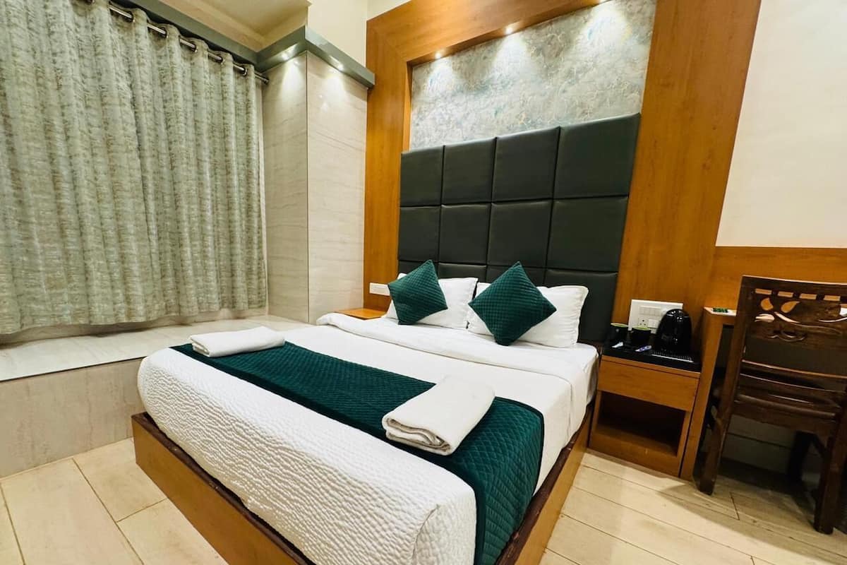 Een hotelkamer met een bed, nachtkastje, stoel en een raam met gordijnen.