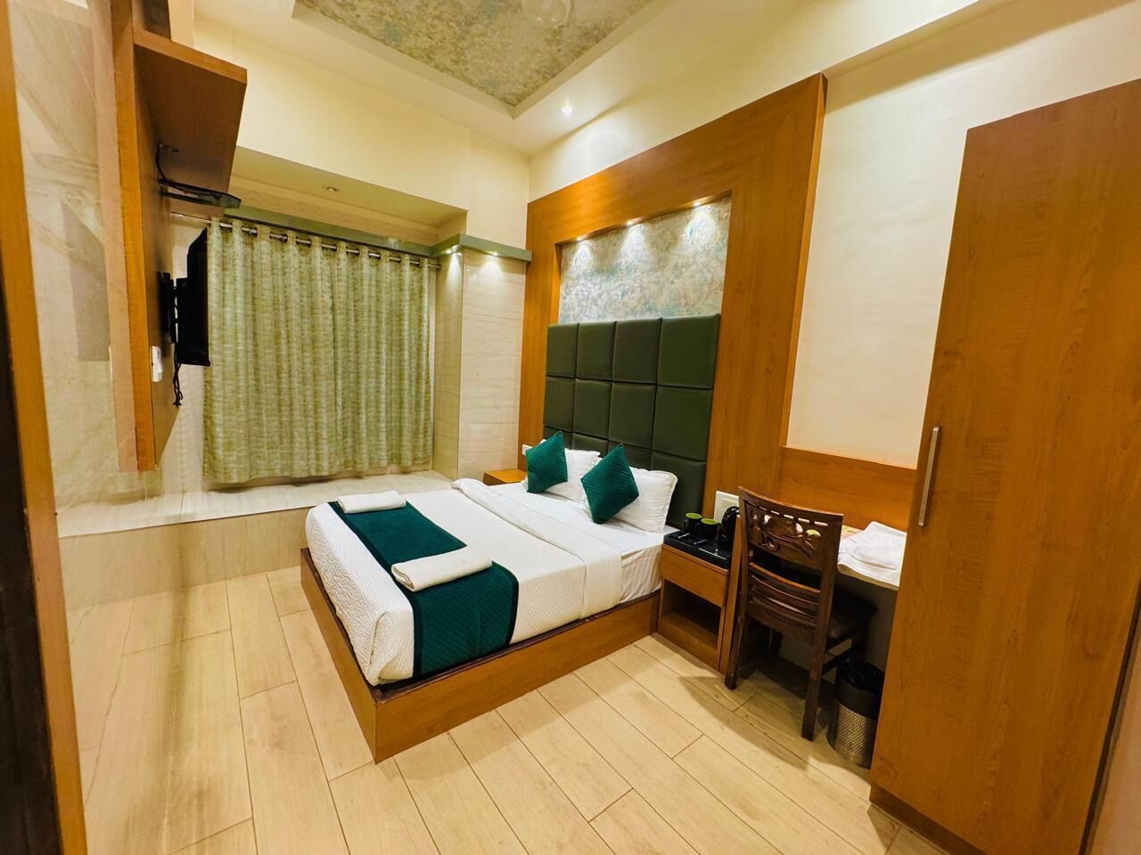 A hotel room with a bed, a desk, a chair, a wardrobe, and a curtain.