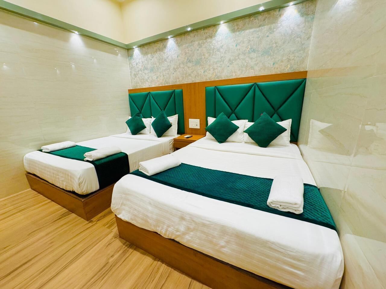 A hotel room with two beds, each with a wooden headboard and green bedding.
