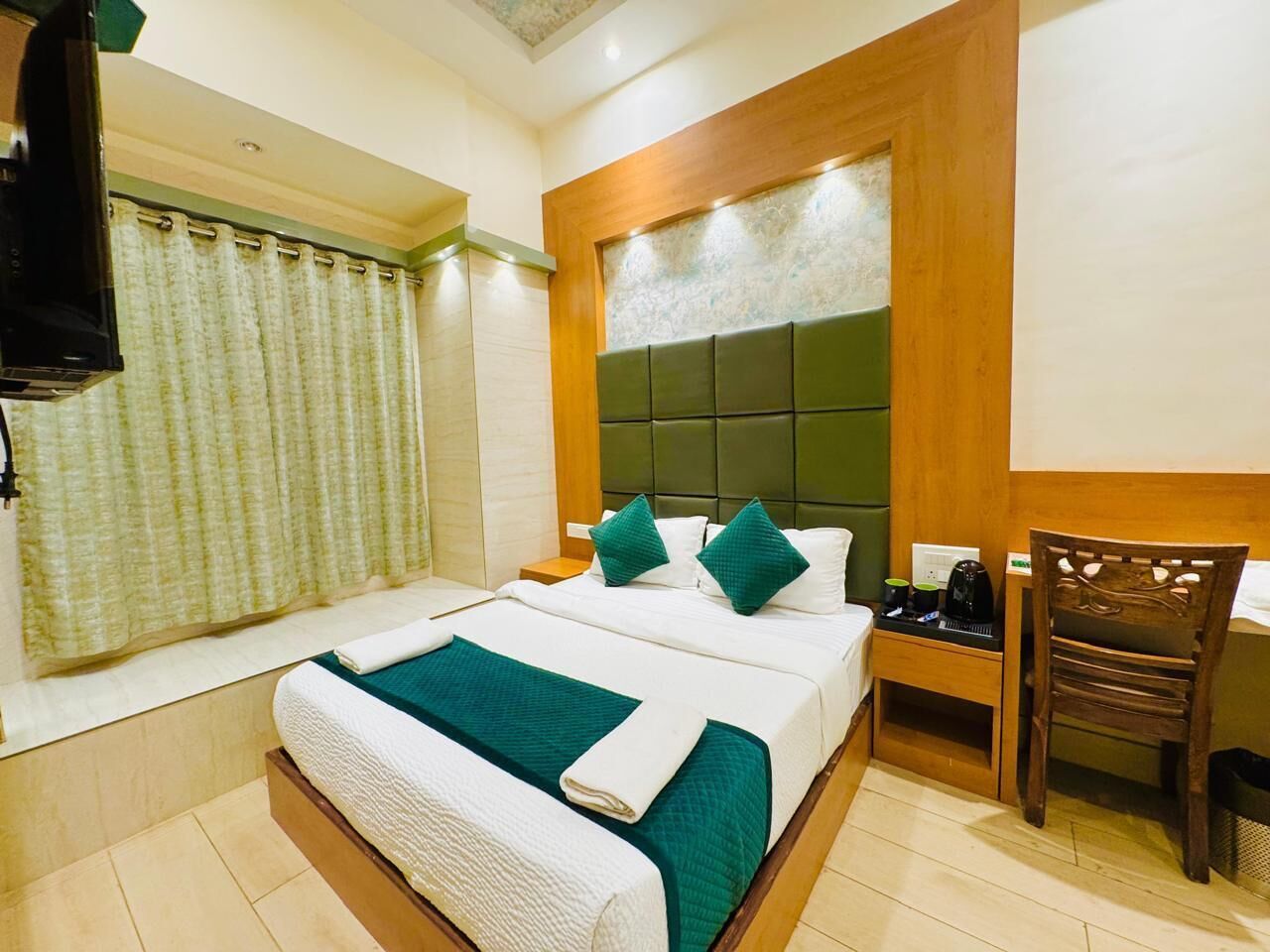A hotel room with a bed, a chair, a nightstand, and a window with curtains.