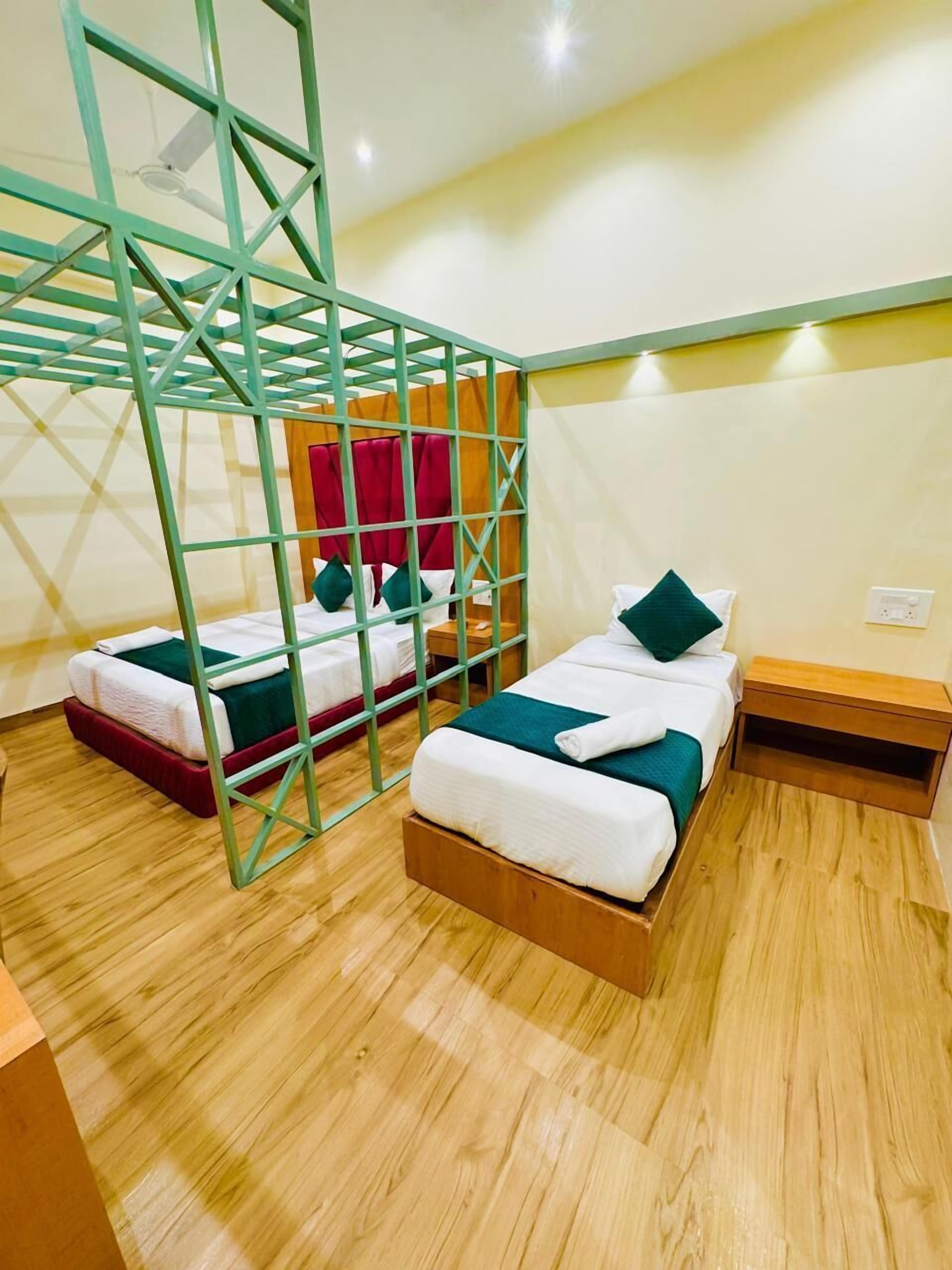 A room with two beds, a wooden floor, a green metal partition, and a red curtain.
