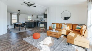 A spacious living area with a sofa, ottoman, and a dining table with chairs. There is a kitchen in the background and a ceiling fan. - Little Haven Cottage: Walk to Meade Tasting (Afton)