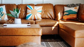 A brown leather sofa with decorative pillows, a small plant, and a book on a matching ottoman. - Little Haven Cottage: Walk to Meade Tasting (Afton)