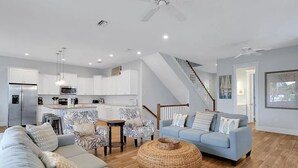 A modern living room with a sofa, a coffee table, and a dining area with a kitchen in the background.