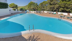 En swimmingpool med hvid kant, liggestole og en bygning i baggrunden.