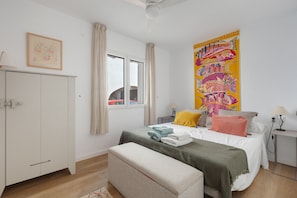 A bedroom with a bed, a bench, a wardrobe, a window, and a colorful tapestry.