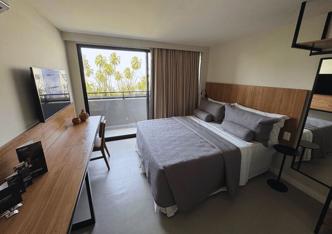 A hotel room with a large bed, a desk, a chair, a small table, and a TV.