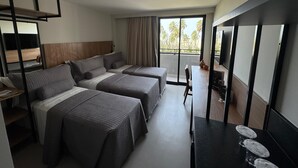 Ein Hotelzimmer mit zwei Betten, einem Schreibtisch, einem Stuhl, einem Fernseher und einem Balkon mit Blick auf Palmen.