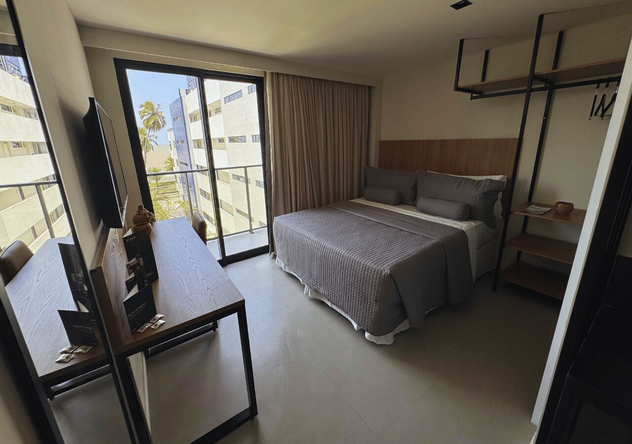 Een hotelkamer met een bed, een bureau, een televisie en uitzicht op palmbomen.