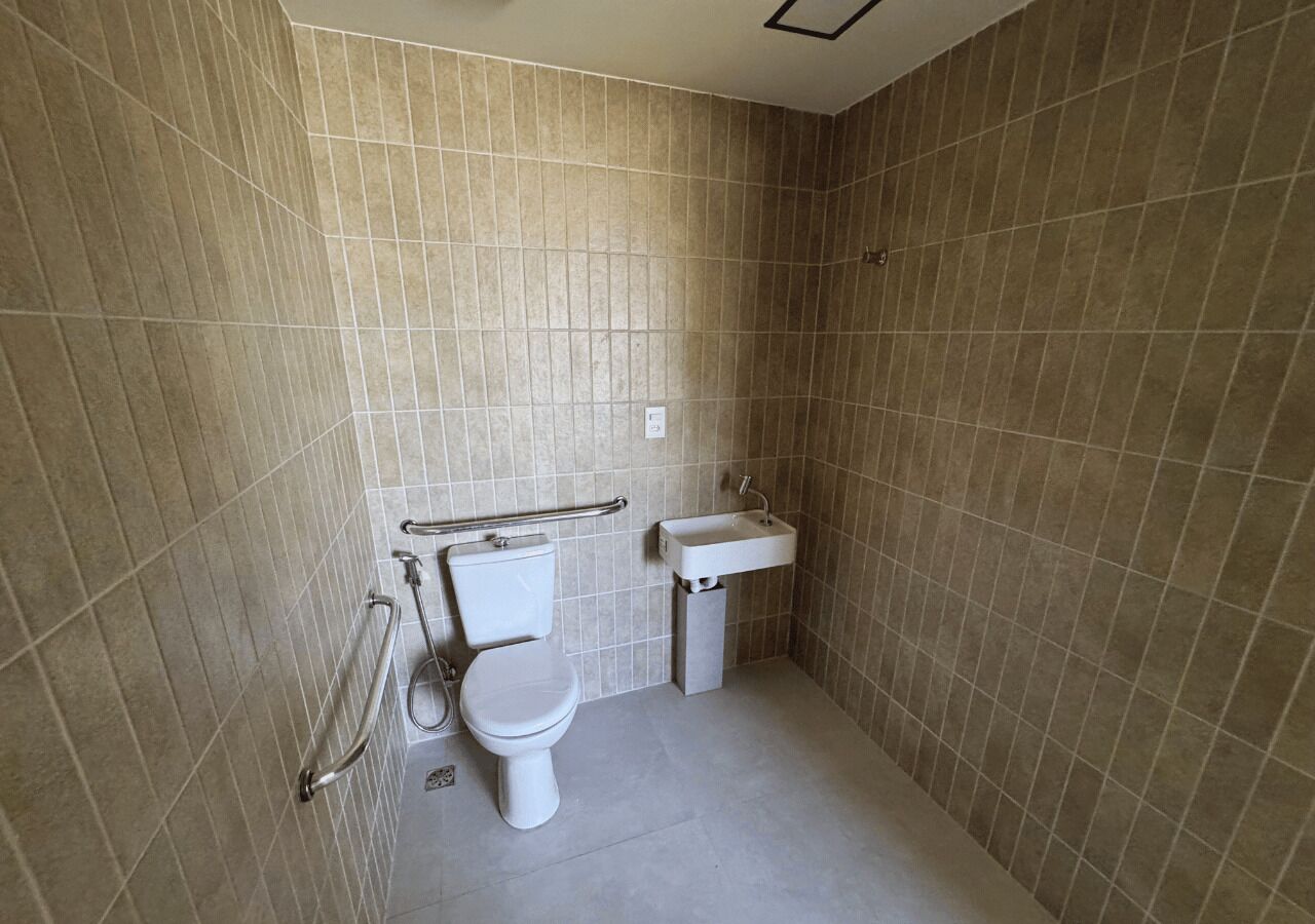 A small, tiled bathroom with a toilet, sink, and grab bars.