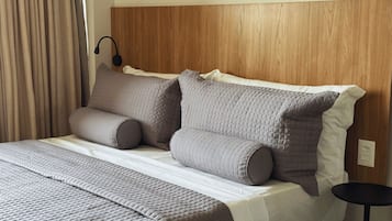 Una cama bien hecha con cabecera de madera, una mesita de noche y una lámpara.