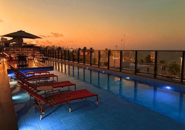 Una piscina al aire libre, sombrillas, sillones reclinables de piscina