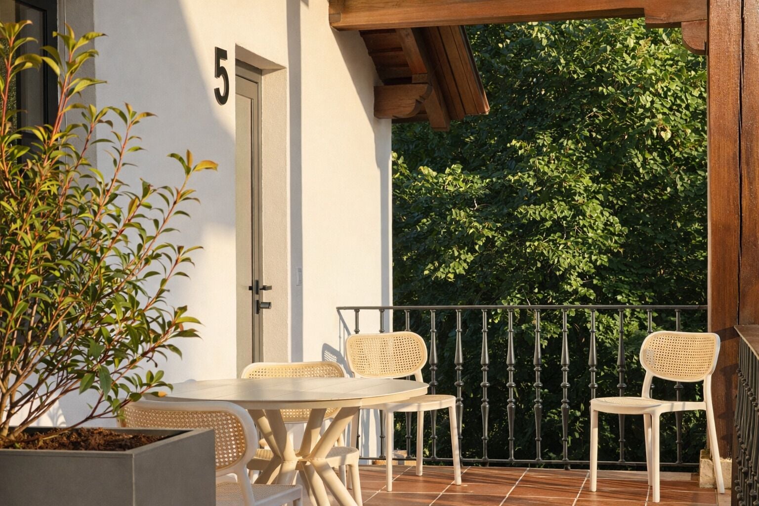 Een balkon met een tafel en stoelen, een bloempot en een deur met het nummer 5.