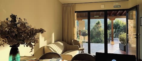 A room with a laptop, papers, a vase with dried flowers, a wicker basket, and a view of the outdoors through a glass door.