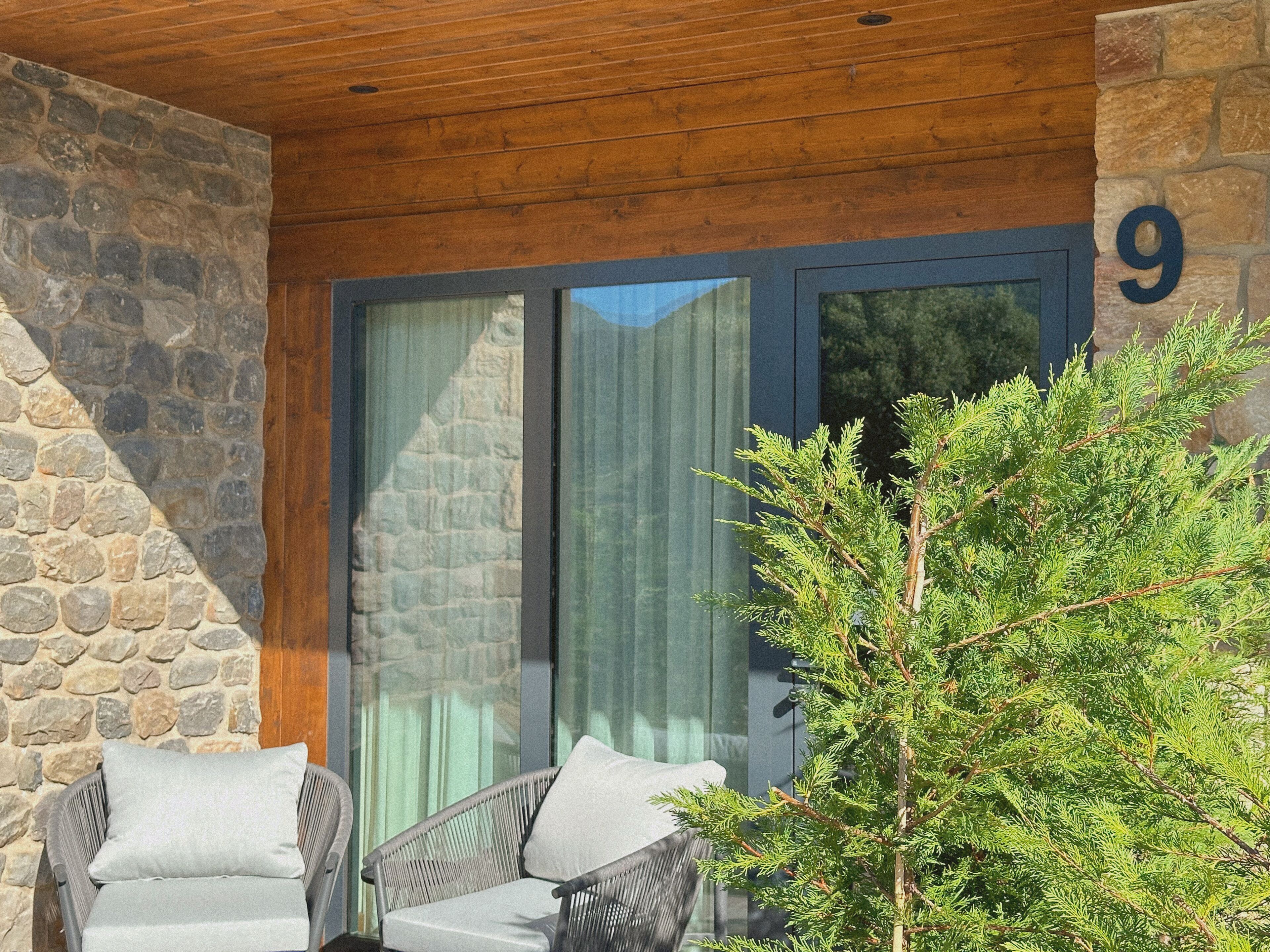 Pared exterior de piedra, techo de madera, puerta de vidrio con cortina y un cartel con el número 9.