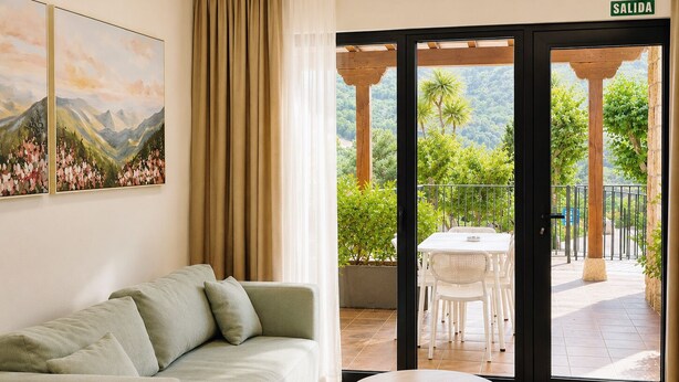 A room with a sofa, a table, and a sliding glass door leading to an outdoor patio with a table and chairs. - El Balcón de Potes  (Potes)