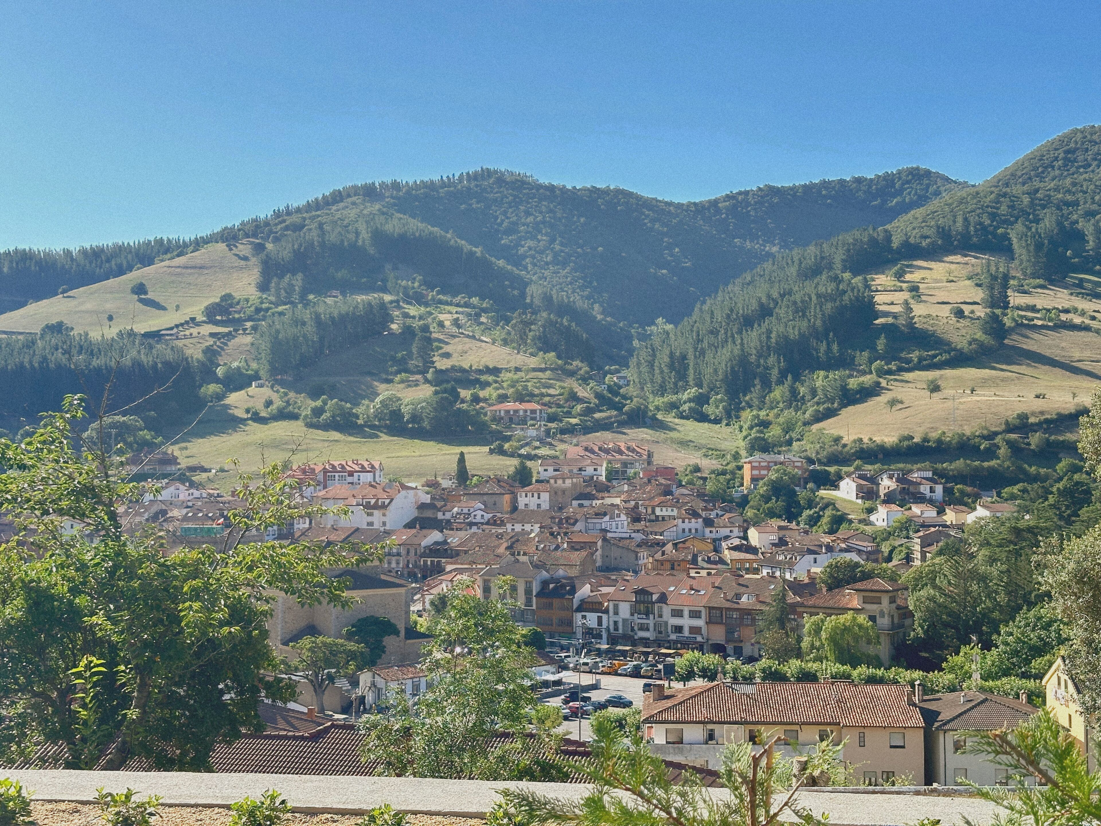 Une ville dont les bâtiments sont entourés de collines et d’arbres.