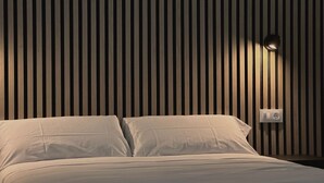 A bed with white linens in a room with vertical wooden paneling and a wall-mounted light fixture. - El Balcón de Potes  (Potes)