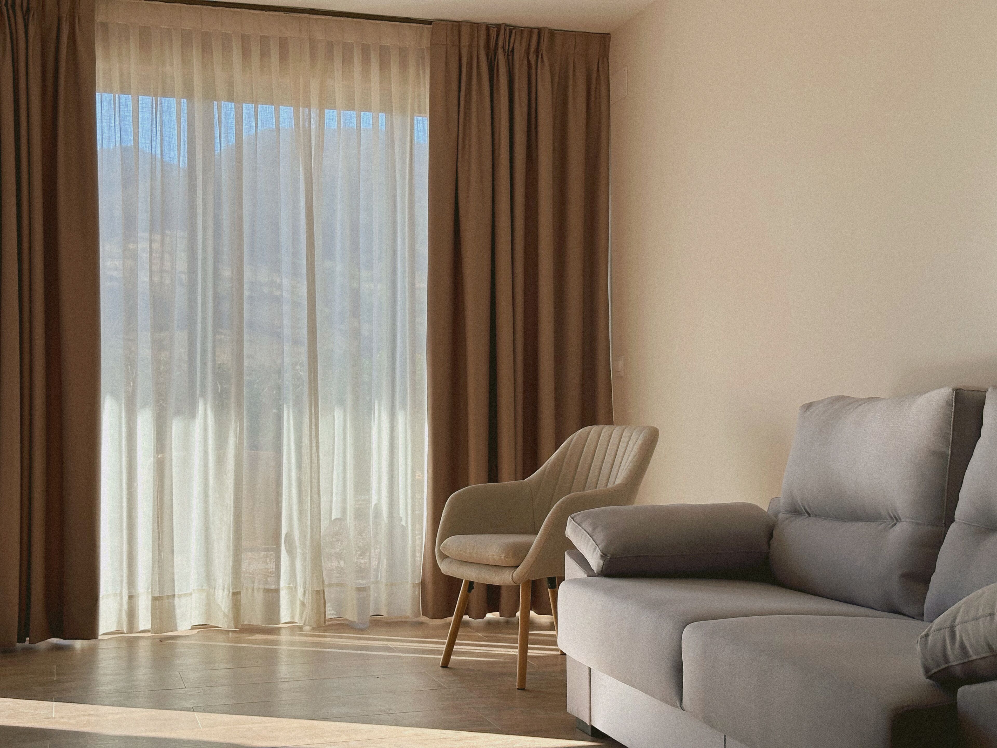 Una sala de estar con un sofá, un sillón y un ventanal con cortinas.