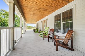 A covered porch with wooden railings, a wooden ceiling, and several Adirondack chairs.