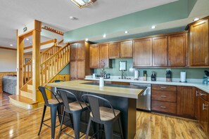 A modern kitchen with wooden cabinets, a central island with bar stools, a built-in dishwasher, and a staircase leading to another level.