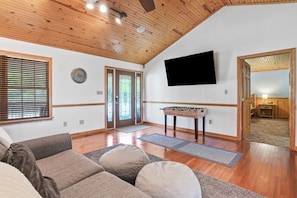 A spacious living room with a wooden ceiling, a sofa, a foosball table, and a television mounted on the wall.