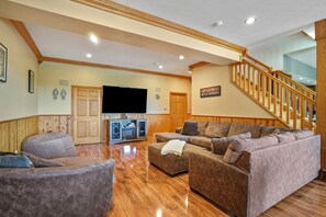 A spacious living room with a wooden staircase, a flat-screen TV, and a large sectional sofa.