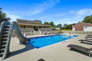 A swimming pool with a slide, lounge chairs, and a covered seating area.