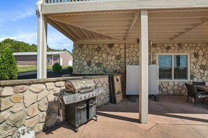 An outdoor patio with a stone wall, a grill, a refrigerator, and a table with chairs.