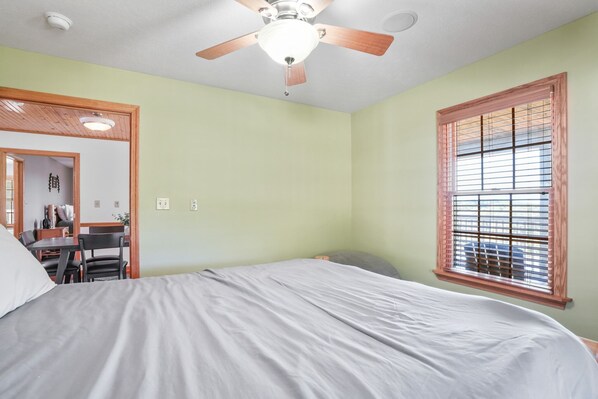 A bedroom with a bed, a ceiling fan, a window with blinds, and a desk area with a chair.