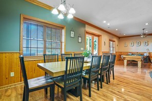 A dining area with a wooden table and chairs, a pool table, and a ceiling fan.