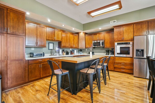 A modern kitchen with wooden cabinets, a central island with bar stools, stainless steel appliances, and recessed lighting.