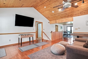 Un grand espace de vie doté d’un plafond en bois, d’un baby-foot, d’un canapé et d’une table de ping-pong.