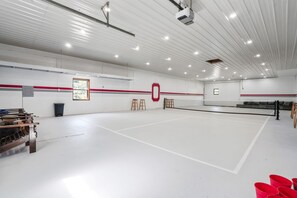 Un court de tennis intérieur équipé d’un filet, de bancs en bois et d’un projecteur fixé au plafond.