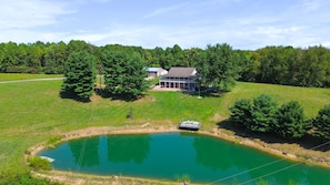 A house with a large pond in front, surrounded by trees and a grassy area.