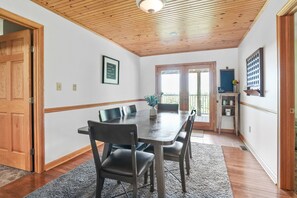 Un espace repas avec un plafond en bois, une table entourée de chaises, un tapis et une porte.