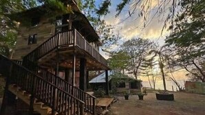 A rustic wooden building with a balcony and a staircase leading to the entrance. - Unique Treehouse Cabin with Ocean Views on West End Negril; Romantic Escape (Westmoreland Parish)