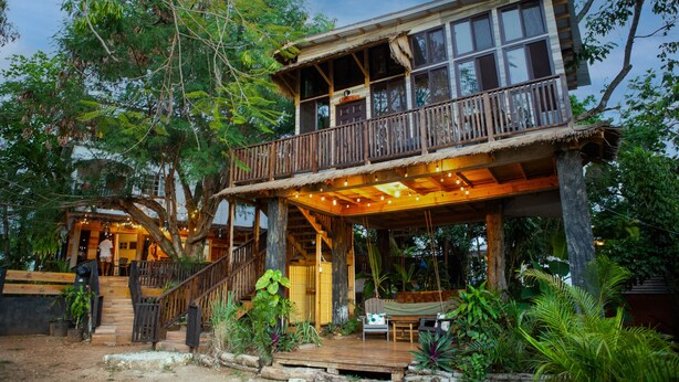 A two-story wooden house with a balcony, surrounded by lush greenery. - Unique Treehouse Cabin with Ocean Views on West End Negril; Romantic Escape (Westmoreland Parish)