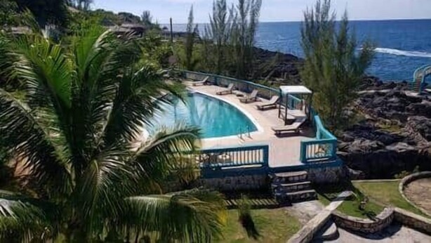 Zona de piscina con sillas de descanso y vista al océano.