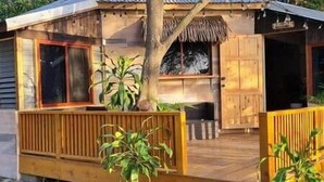 Una cabaña de madera con una puerta grande abierta, una ventana y un pequeño porche con plantas en macetas.