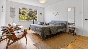 A bedroom with a bed, a chair, a small table, a hanging light fixture, and a window with a view of trees. - Two Bedroom Home Near the Freeway for Easy Access (San Francisco)
