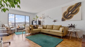 A modern living room with a large sectional sofa, a small round table, and a view of the city through large windows. - Two Bedroom Home Near the Freeway for Easy Access (San Francisco)