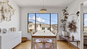 A modern kitchen with a large dining table, white cabinetry, and a view of houses through large windows. - Two Bedroom Home Near the Freeway for Easy Access (San Francisco)