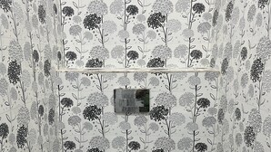 A bathroom with a toilet, a shower, and a wall with floral tile patterns.