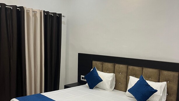 A modern hotel room with a large bed, a headboard with a tufted design, and a curtain on the window.