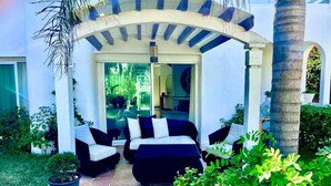 An outdoor seating area with a sofa and chairs, surrounded by greenery and a palm tree. - Villa au calme, jardin spacieux et confort moderne (Skhirat)