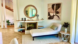 A living room with a fireplace, a sofa, a round mirror, and abstract wall art. - Villa au calme, jardin spacieux et confort moderne (Skhirat)