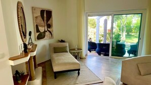 A spacious living room with a large window, a sofa, a small table, and a decorative mirror. - Villa au calme, jardin spacieux et confort moderne (Skhirat)